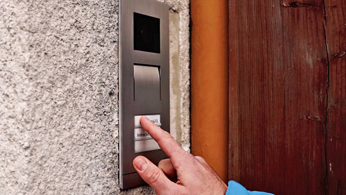 Ruka tiskne tlačítko na domovním zvonku s kamerou